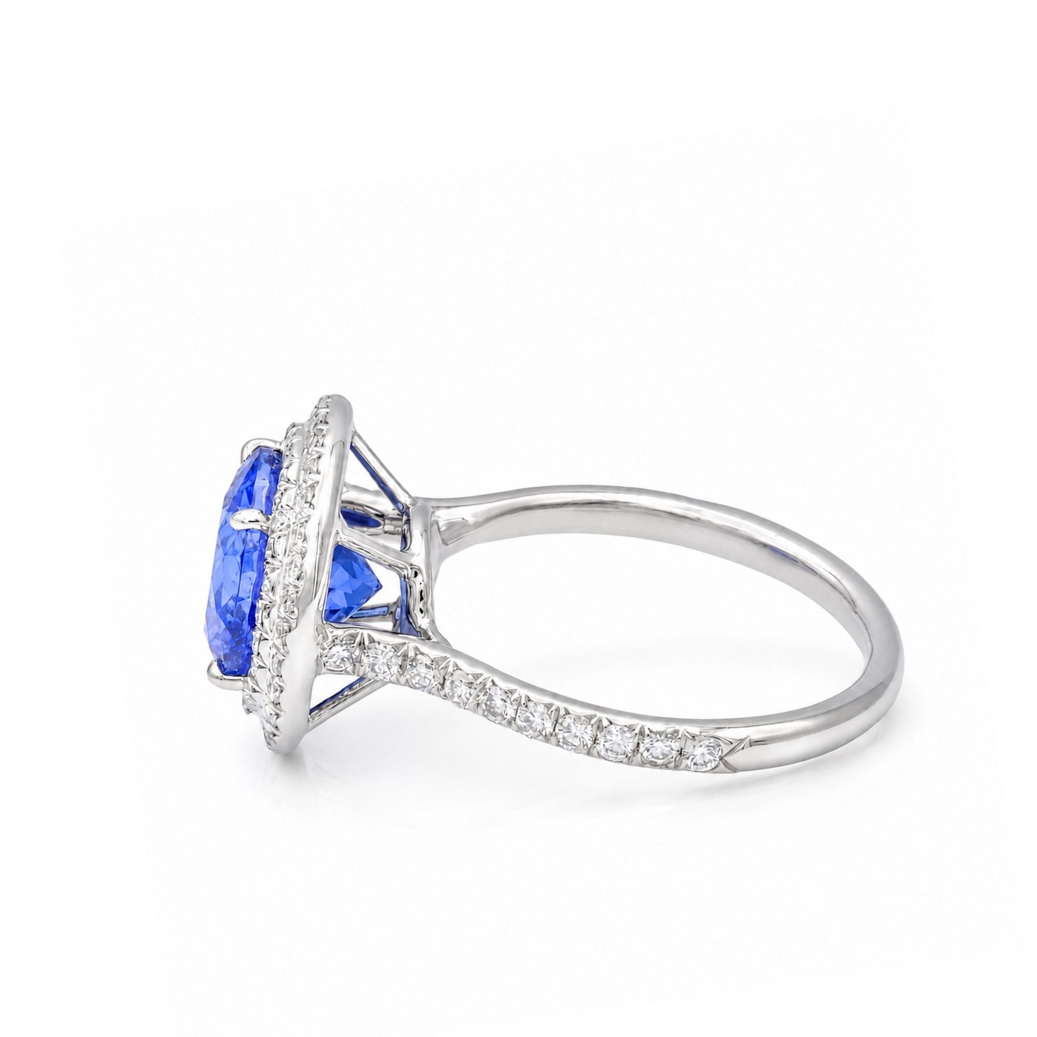 A silver-toned tanzanite ring featuring a large oval-cut blue gemstone in a halo setting, with a pavé band accented by small round stones, shown on a white background.